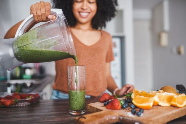 Eine Frau gießt einen grünen Smoothie in ein Glas