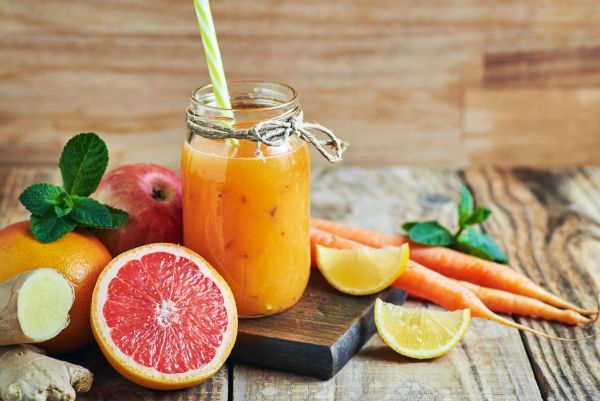Ein oranger Smoothie in einem Glas mit Obst drum herum
