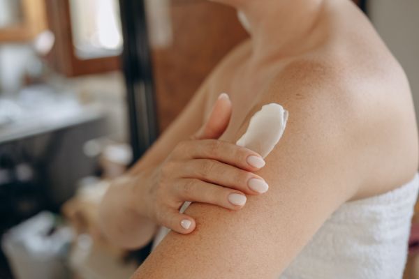 Eine Frau streicht Creme auf ihre Schulter