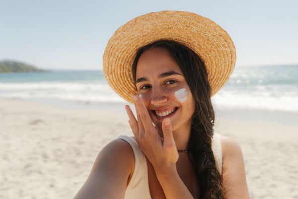 Eine Frau mit Sonnenhut und Creme auf den Wangen am Strand