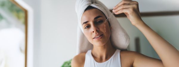 Eine Frau träufelt mit einer Pipette Gel auf ihre Wange