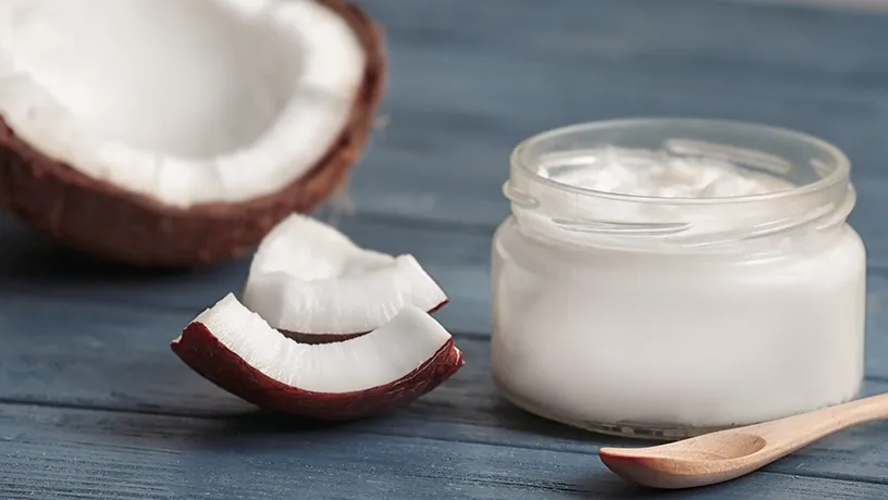 Stücke einer Kokosnuss mit einem Tiegel Kokosnussöl