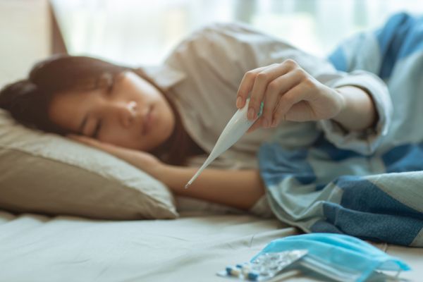 Eine Frau liegt im Bett und betrachtet ein Fieberthermometer