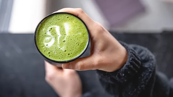 Eine Hand hält eine Tasse mit einem grünem Matcha Getränk