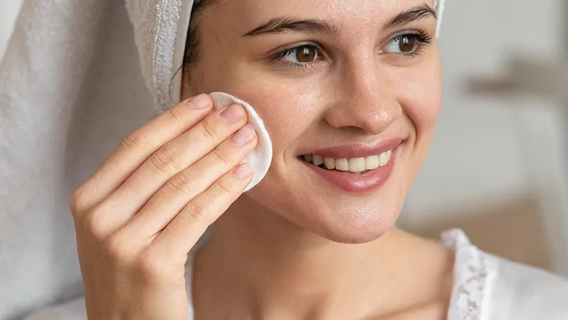 Eine Frau mit Handtuchturban reibt mit einem Wattepad über ihre Wange