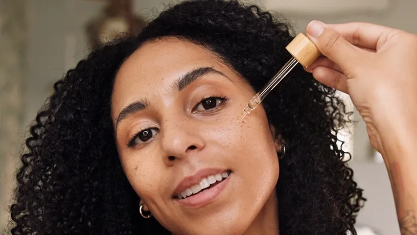 Eine Frau mit langen schwarzen Haaren träufelt mit einer Pipette Peptide auf ihre Wange